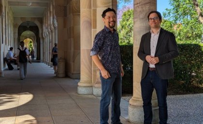 two  men stand by a pillar in a shady stone walkway